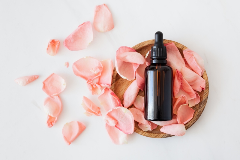 Composition of cosmetic bottle with pink rose petals and wooden plate The Ultimate Guide to Mānuka Oil Dilution www.manukaoil.com