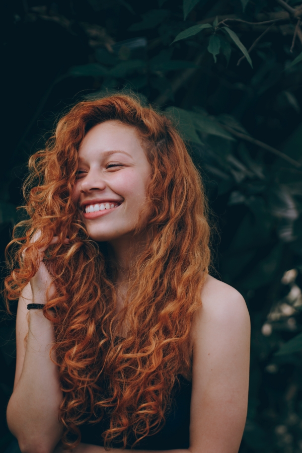 girl with red curly long hair smiling 7 Ways to Maintain Healthy Hair with Mānuka Oil www.manukaoil.com 