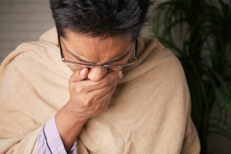 man in sweater wearing black eyeglasses with an allergy sneezing www.manukaoil.com