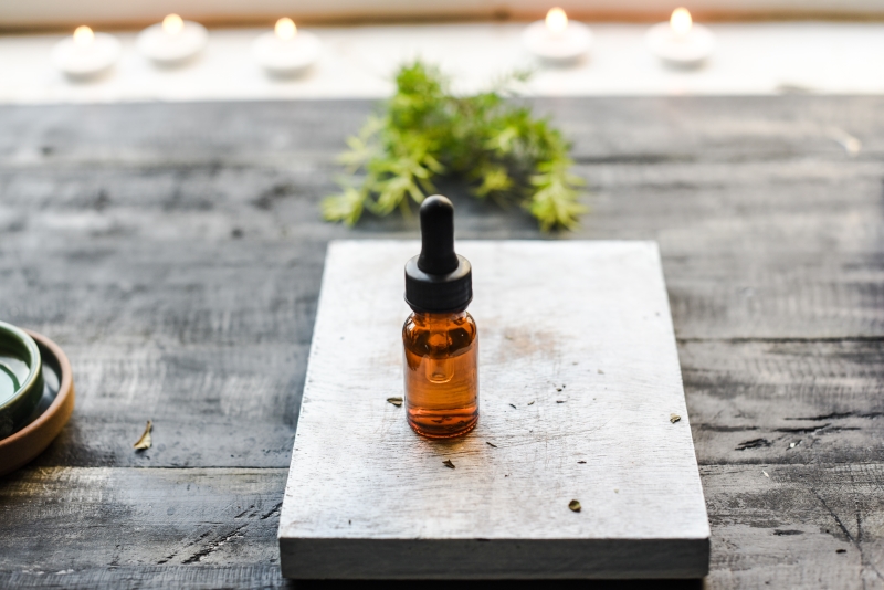 A bottle of manuka essential oil with dropper on a wooden background with candles